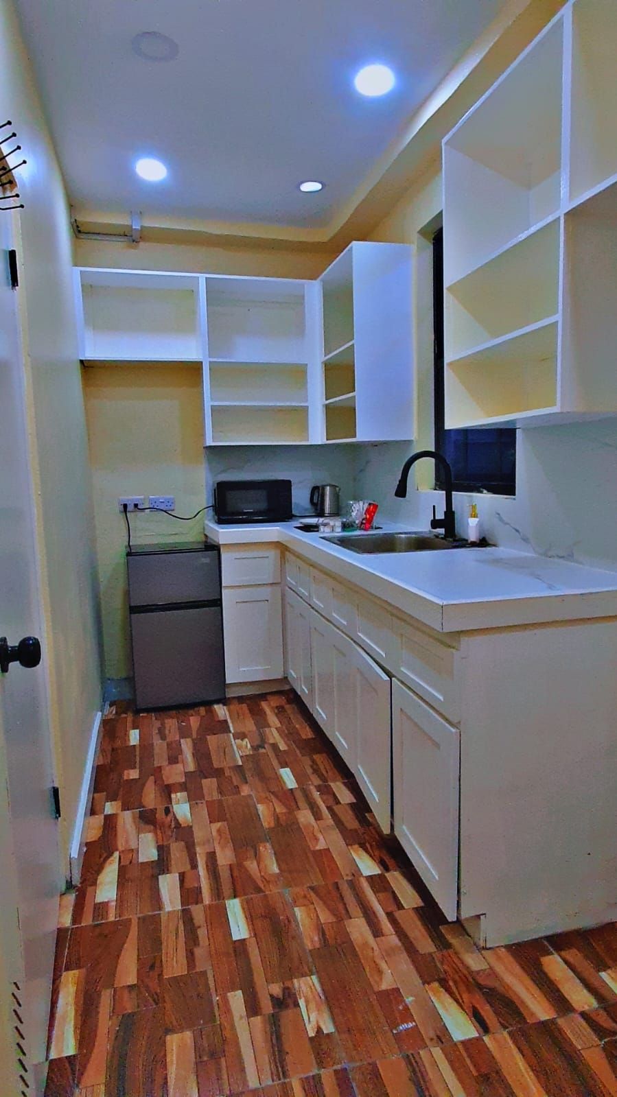 A compact kitchen with white cabinets, a microwave, a sink, and a refrigerator.