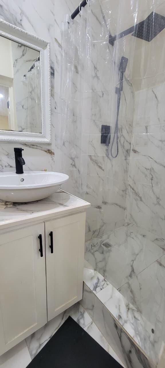 Baño con lavamanos blanco, espejo y zona de ducha.