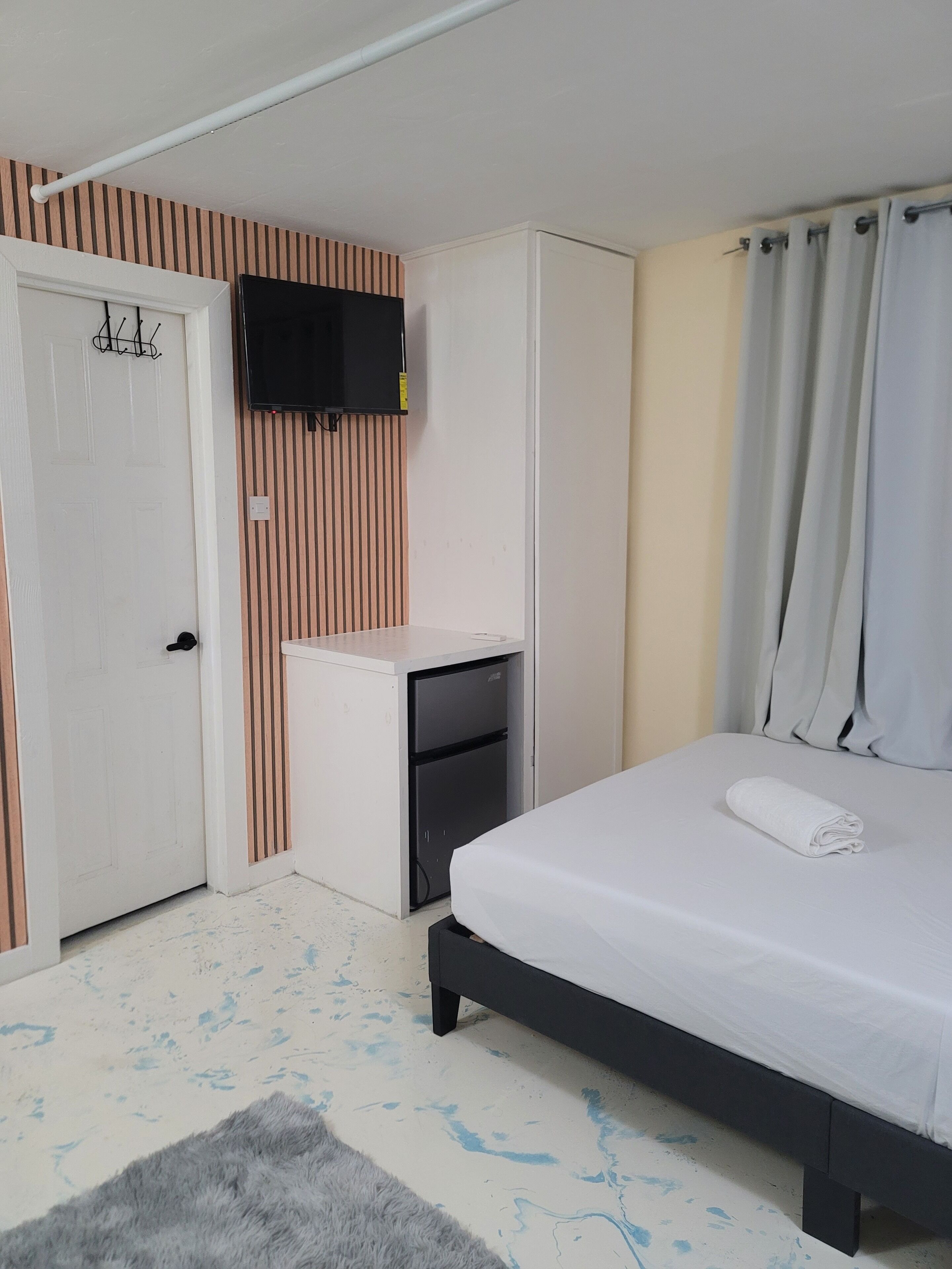 A bedroom with a bed, a desk, a television, and a door.