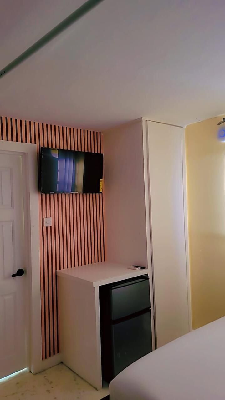 A room with a bed, a television mounted on a slanted wall, a small desk with a computer, and a door.