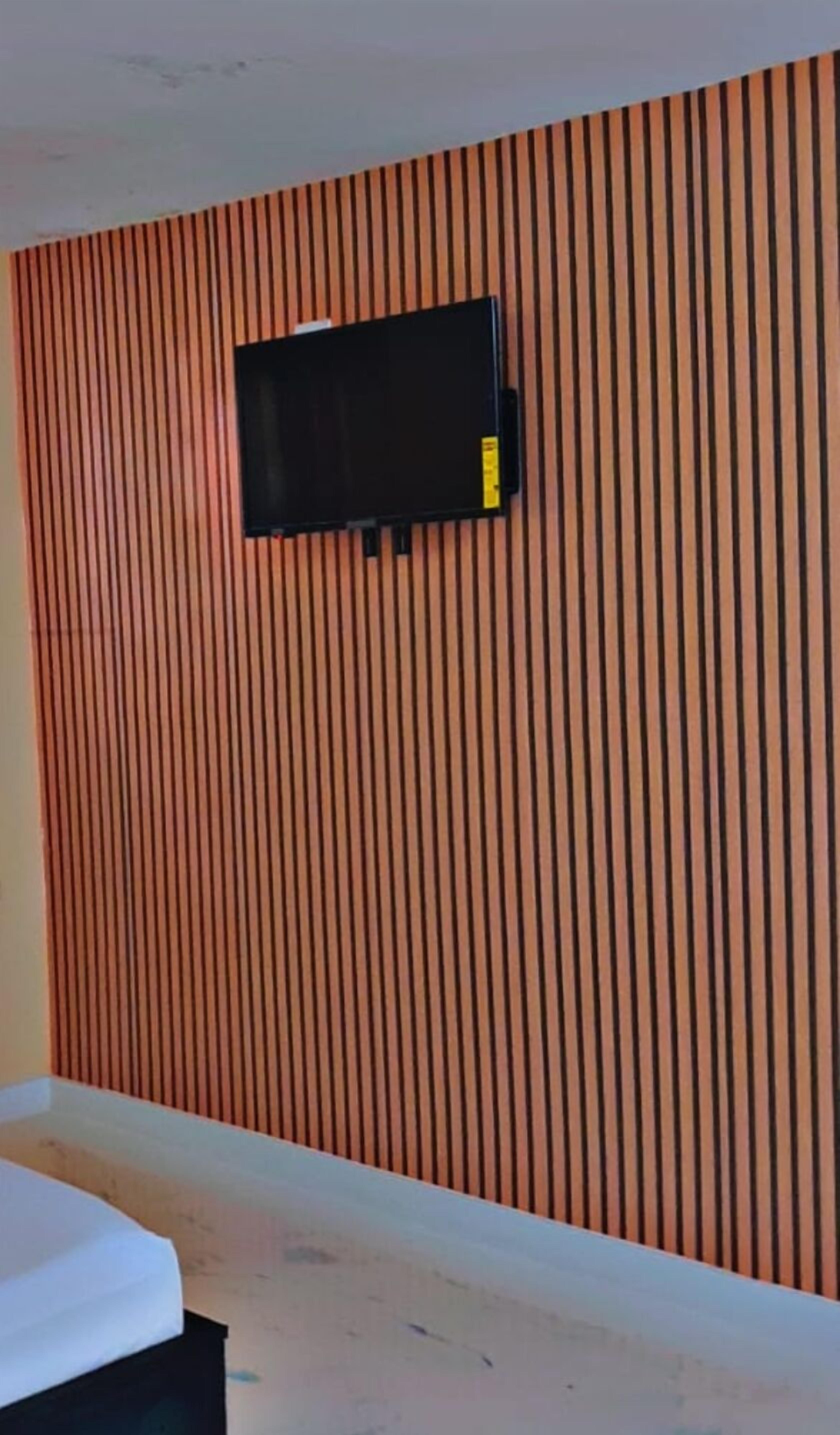 Una stanza con un letto, una TV a schermo piatto montata su un pannello a listelli e un soffitto bianco.