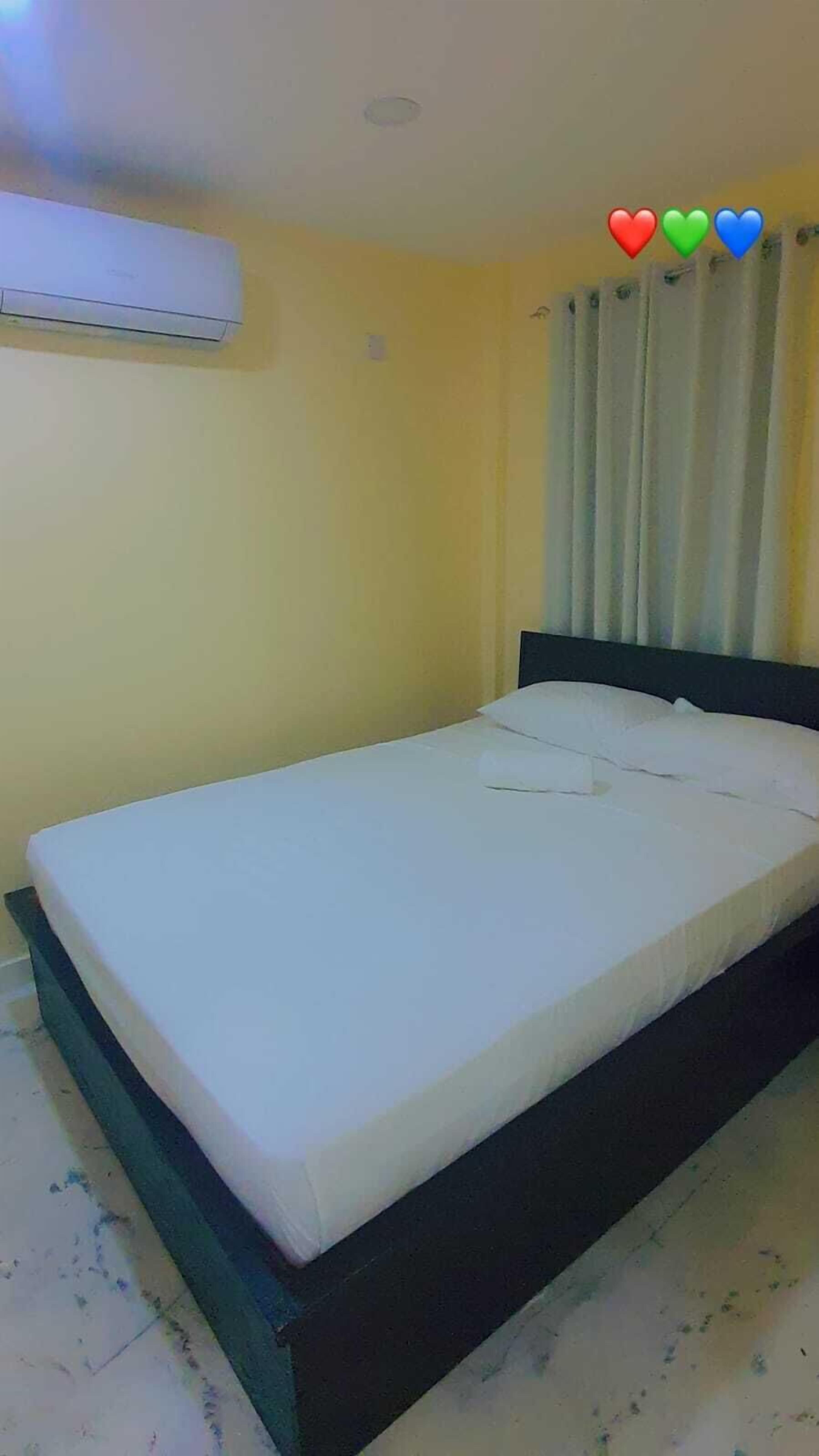 A single-bed room with a white mattress, a black headboard, and a yellow wall.