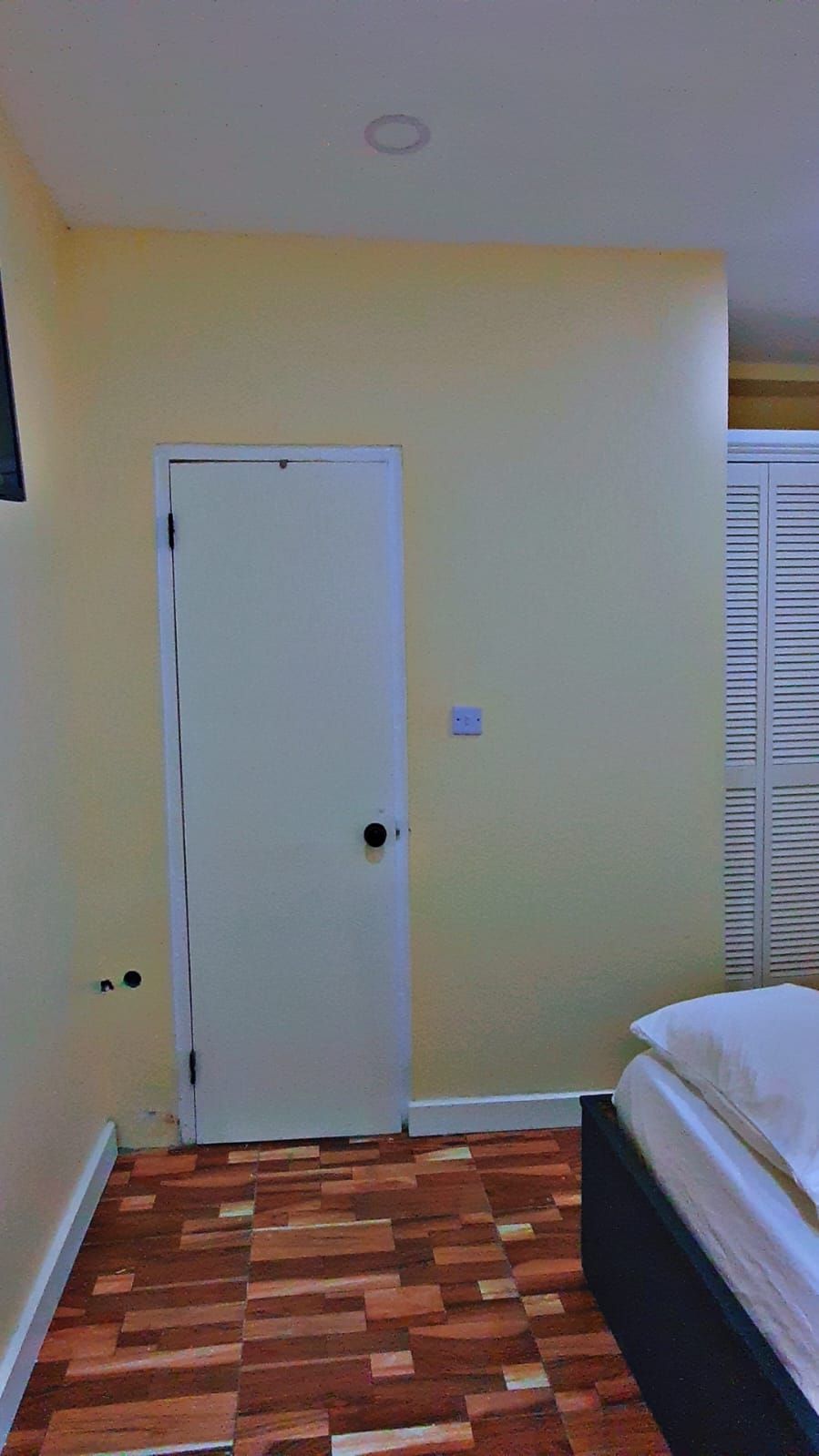 Una stanza con pavimento in legno, una porta bianca e un letto con biancheria da letto bianca.