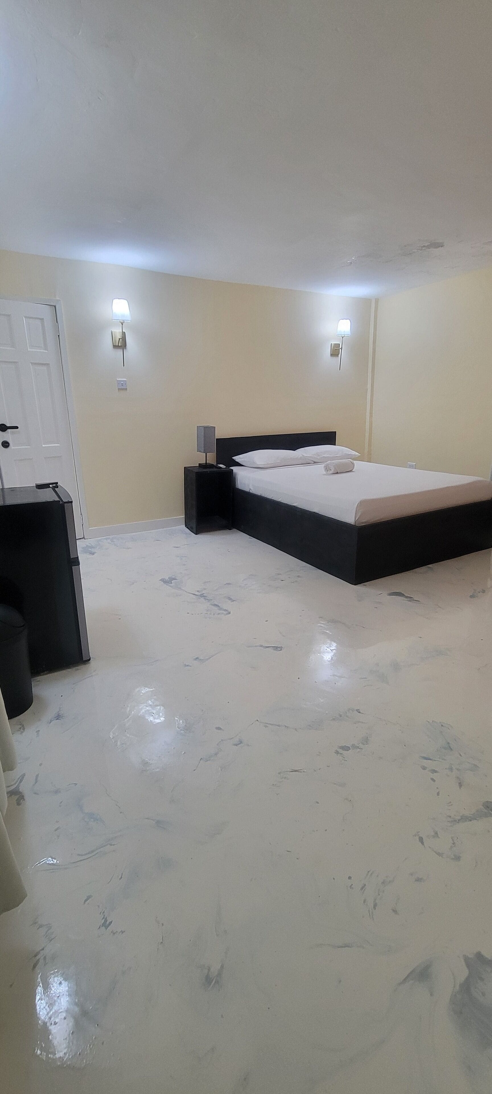 A bedroom with a bed, bedside tables, a wall-mounted light, and a door.