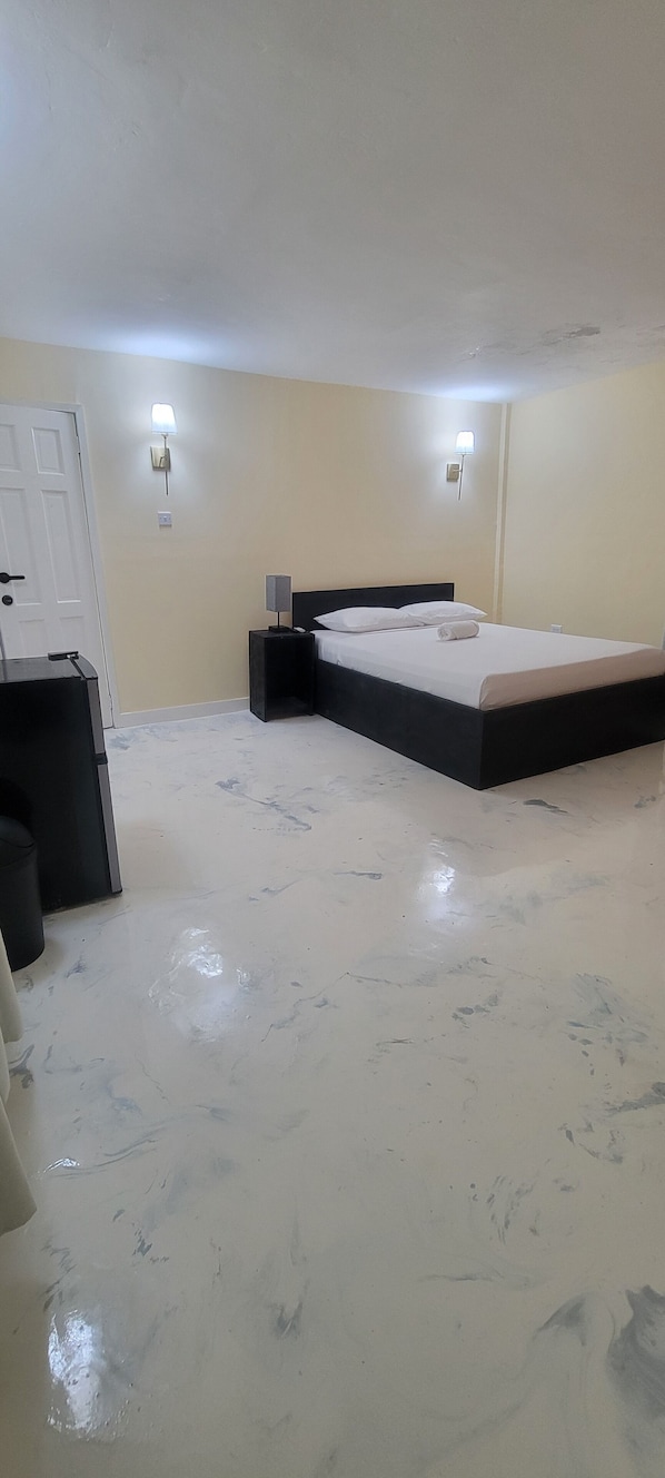 A bedroom with a bed, bedside tables, a wall-mounted light, and a door.