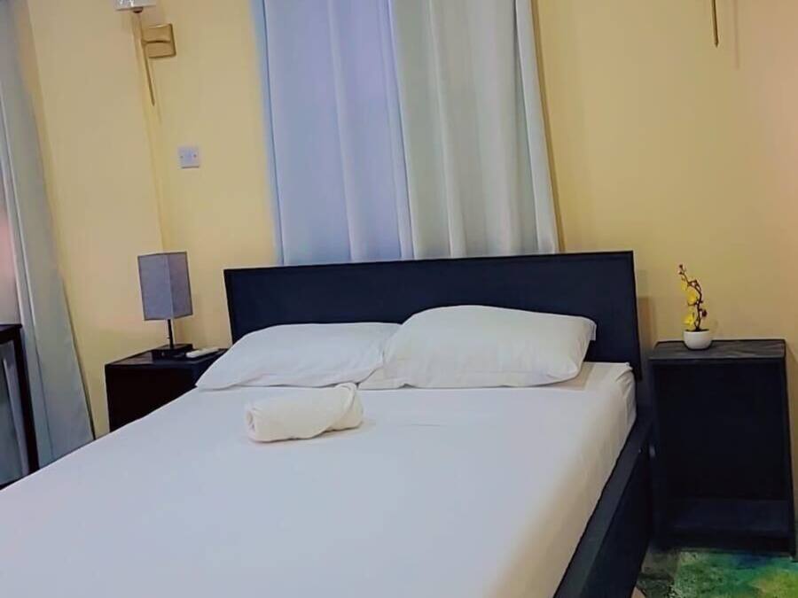 Una habitación de hotel con cama, mesita de noche, lámpara y luz empotrada en la pared.