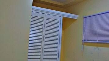Une petite pièce avec une armoire blanche, une fenêtre avec des stores et un luminaire au plafond.