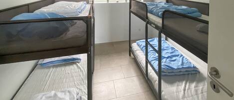 A dormitory room with bunk beds, a window with a view of greenery, and a door with a handle.