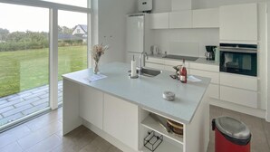 A modern kitchen with a large window, white cabinets, a built-in oven, and a red trash bin. - Pet friendly home in Allingåbro with sauna (Allingåbro)