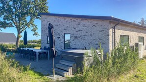 A modern building with a brick exterior, outdoor seating area, and a hot tub. - Pet friendly home in Allingåbro with sauna (Allingåbro)
