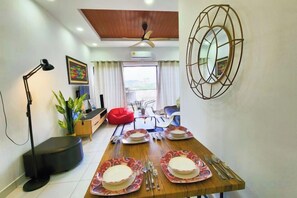 Un comedor con una mesa de madera dispuesta para cuatro, un ventilador de techo y un espejo decorativo en la pared.