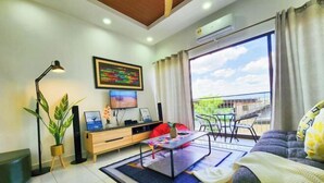 Un salon moderne comprenant un canapé, une table basse, un téléviseur et un balcon aménagé avec du mobilier d’extérieur.