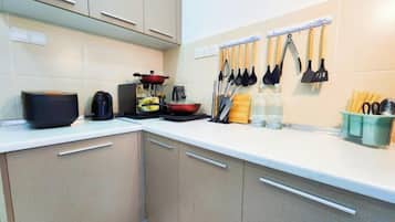 A kitchen with cabinets, a countertop, a kettle, a frying pan, and utensils hanging on the wall.