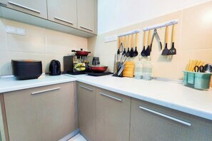 Una cocina con armarios, una encimera, un hervidor, una sartén y utensilios colgados en la pared.
