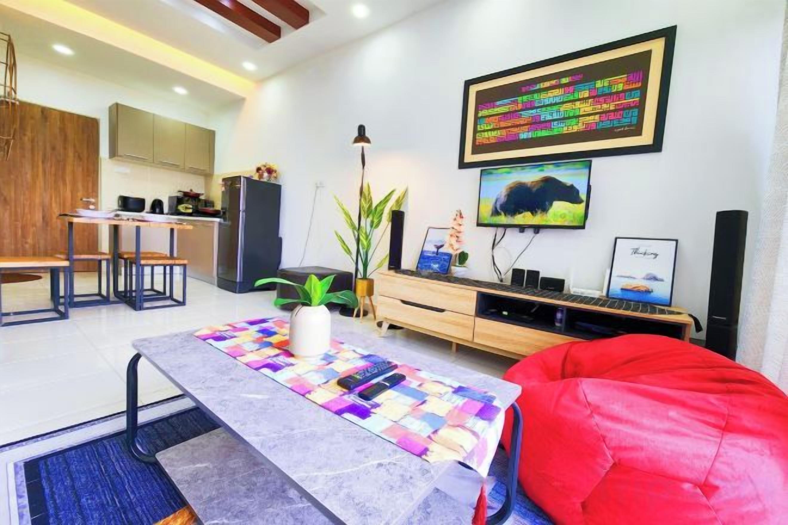 A modern living room with a dining area, a TV, and a kitchen in the background.