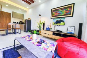 A modern living room with a dining area, a TV, and a kitchen in the background. - KLIA Lili Residensi 5+2 PAX with Splendid Pool (Nilai)