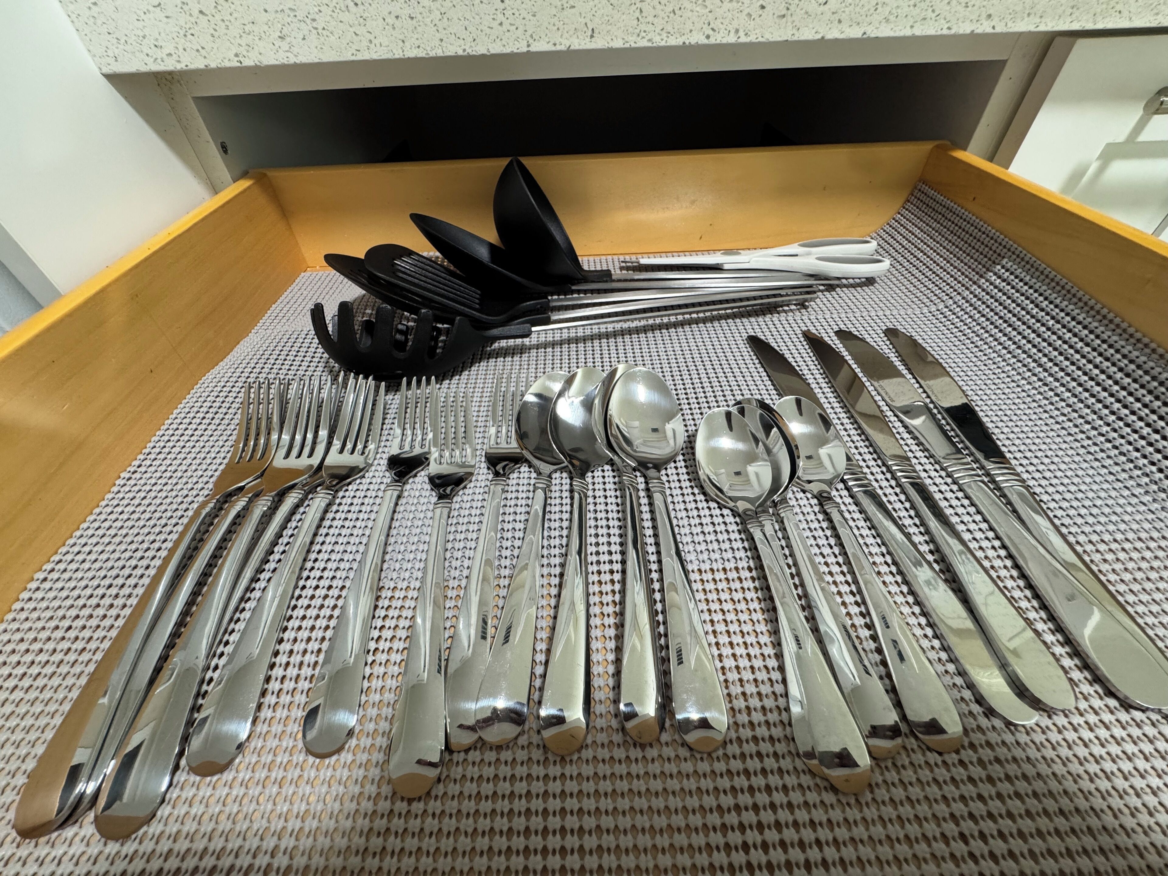 A drawer containing a set of silverware, including forks, knives, spoons, and a black spatula.