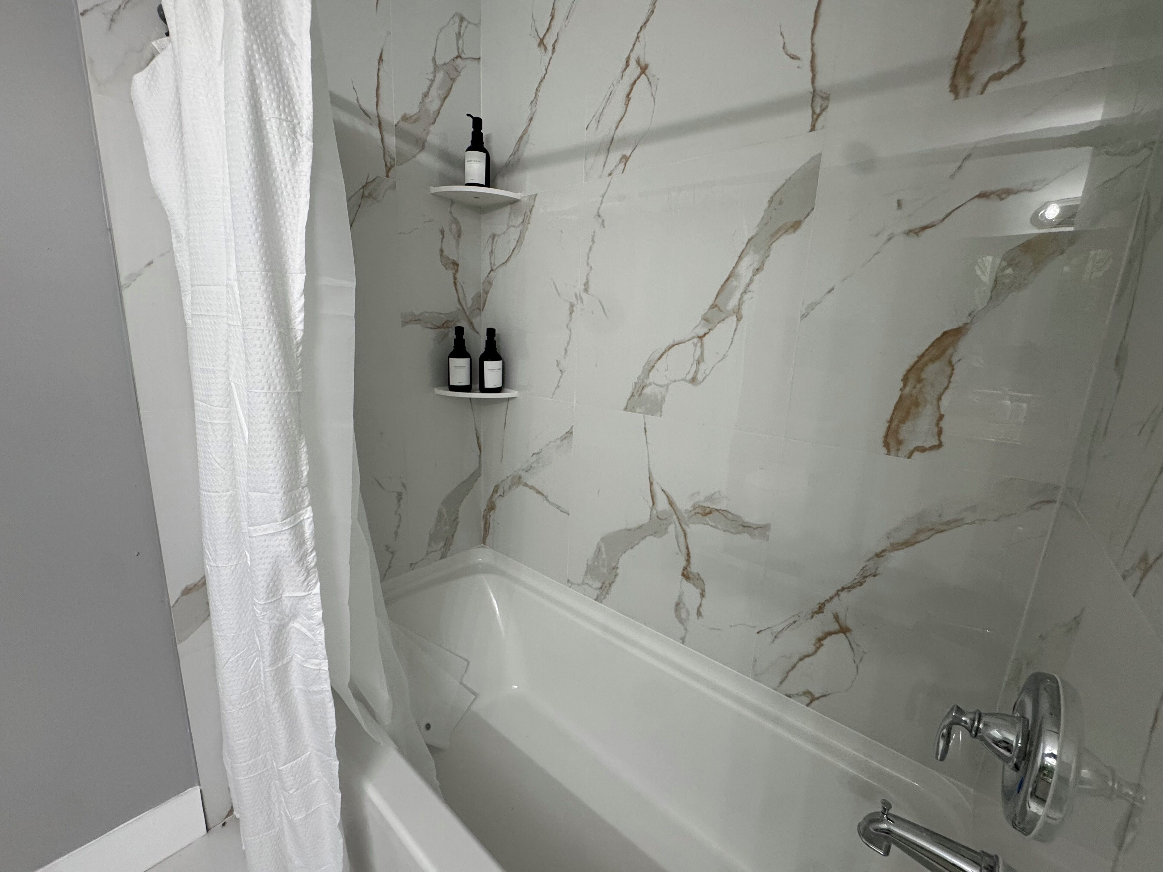 A bathroom with a marble wall, a bathtub, and two shelves with bottles.