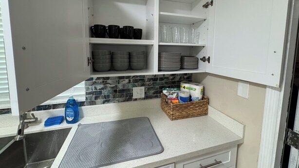 Cozinha com armários brancos, painel de azulejos e bancada com um frasco de detergente e uma esponja.