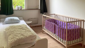 Un dormitorio con una cama, una cuna, un radiador y una ventana con cortinas.