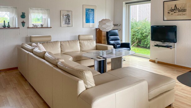 Una sala de estar moderna con un sofá seccional color beige, una mesa de centro y un televisor sobre un mueble.