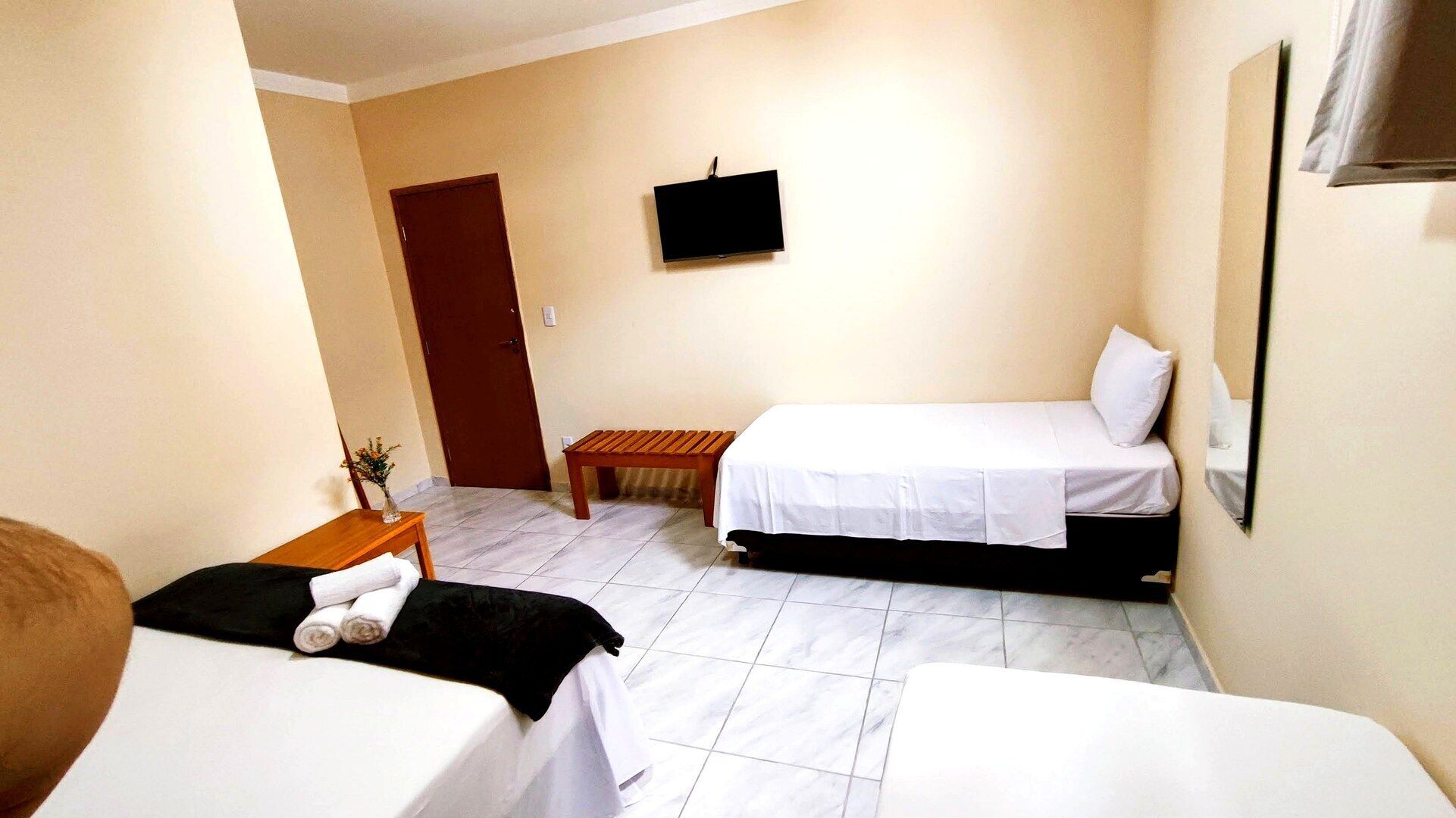 Habitación de hotel con dos camas, una mesita de madera, un televisor fijado a la pared y una puerta.