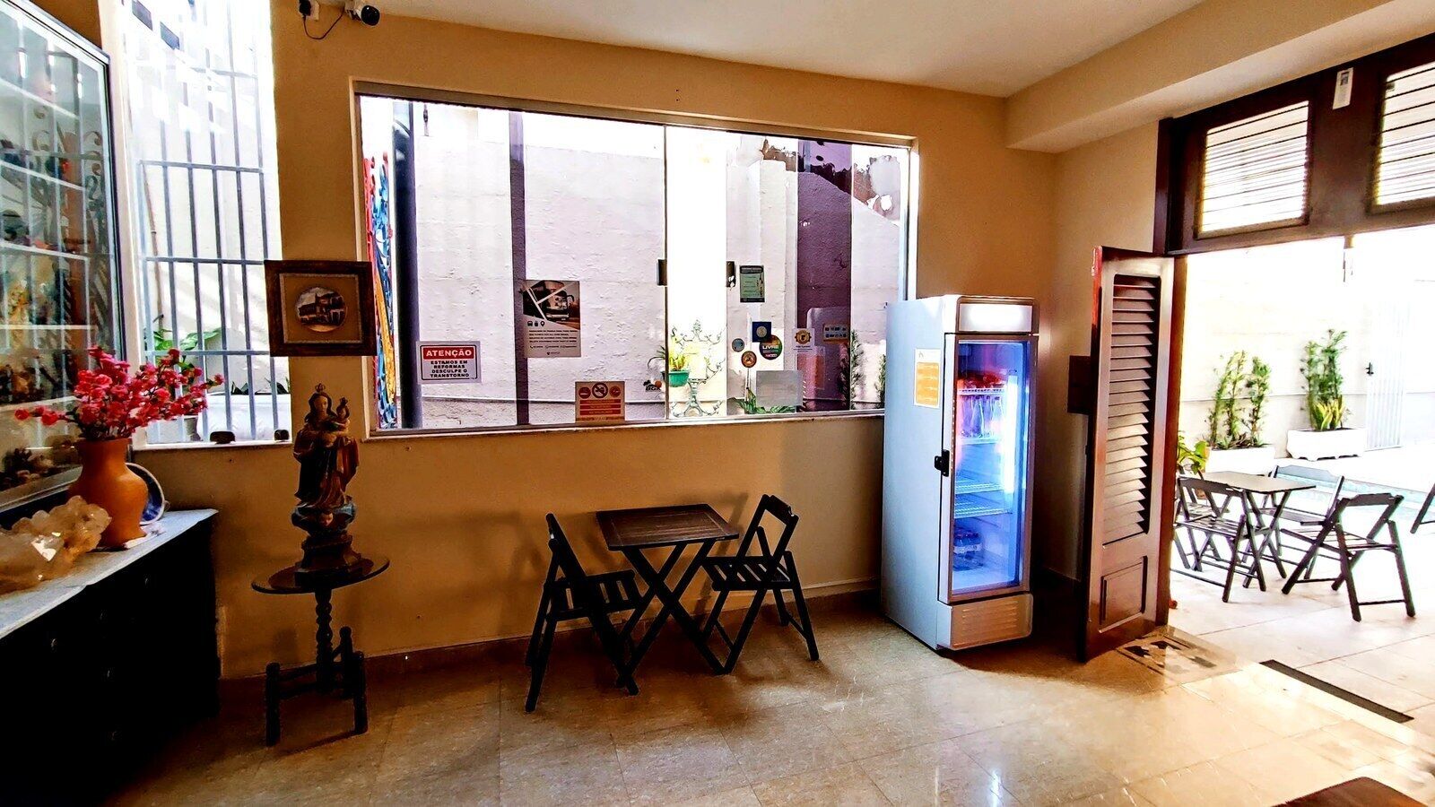 Una habitación con ventana, refrigerador, una mesa con sillas y una pequeña estatua sobre una mesa.