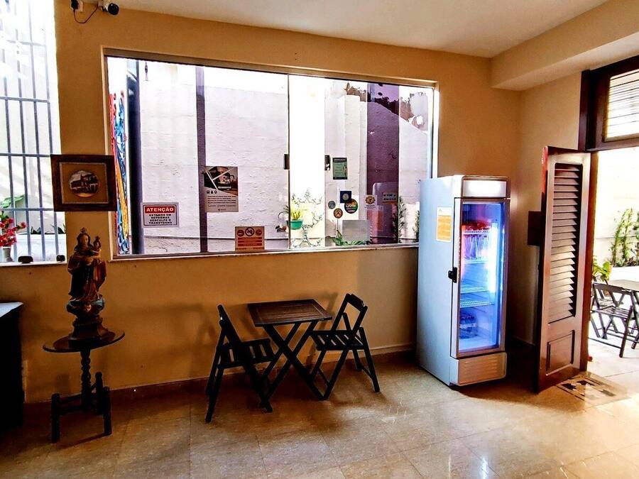 Una habitación con ventana, refrigerador, una mesa con sillas y una pequeña estatua sobre una mesa.