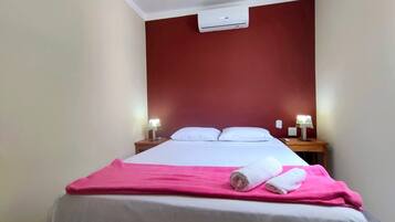 Habitación de hotel con cama, dos mesitas de noche con lámparas, una pared de acento roja y un equipo de aire acondicionado.