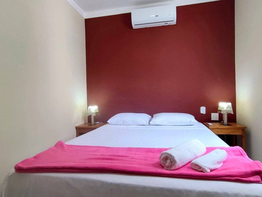 Habitación de hotel con cama, dos mesitas de noche con lámparas, una pared de acento roja y un equipo de aire acondicionado.