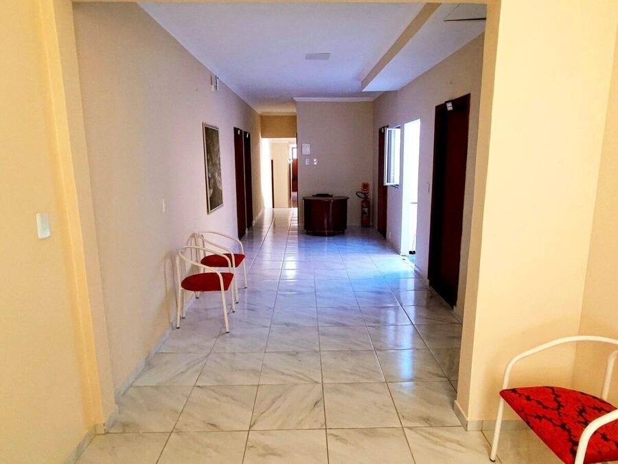 A hallway with a tiled floor, two white chairs with red cushions, and a red cushion on a white chair.