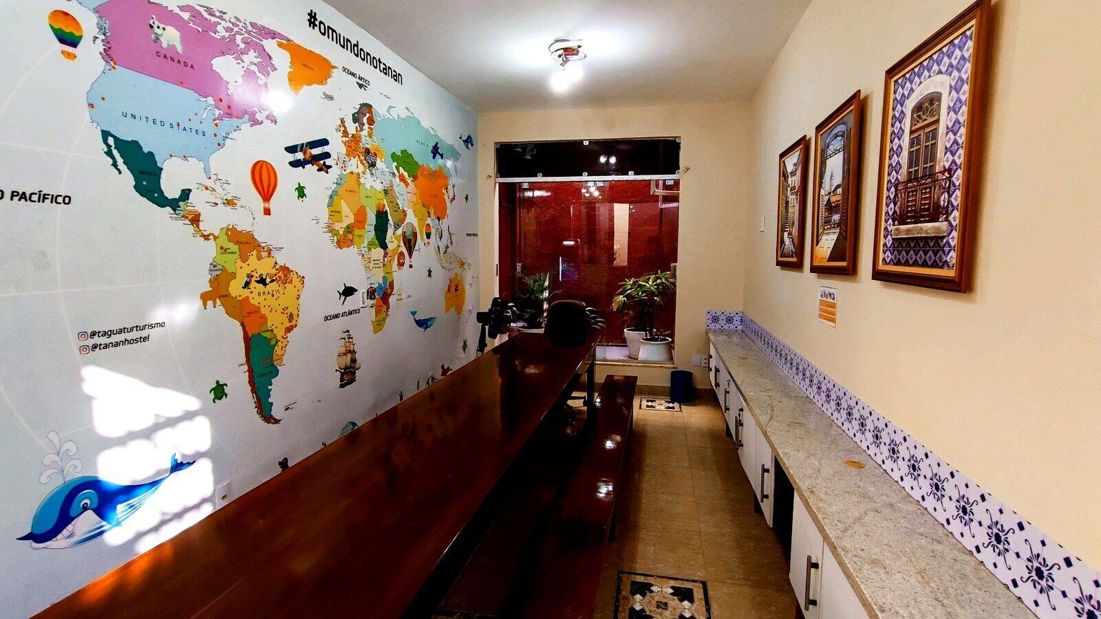 Un vestíbulo de hotel con un mural de un mapa mundial, una recepción y obras de arte enmarcadas en la pared.