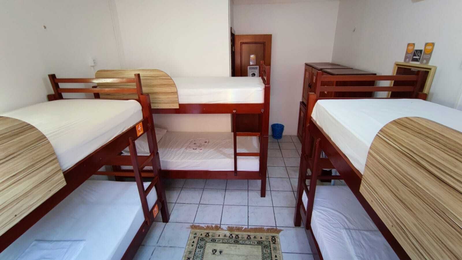 Une pièce comprenant quatre lits superposés en bois, un petit bureau et une porte donnant sur une autre pièce.