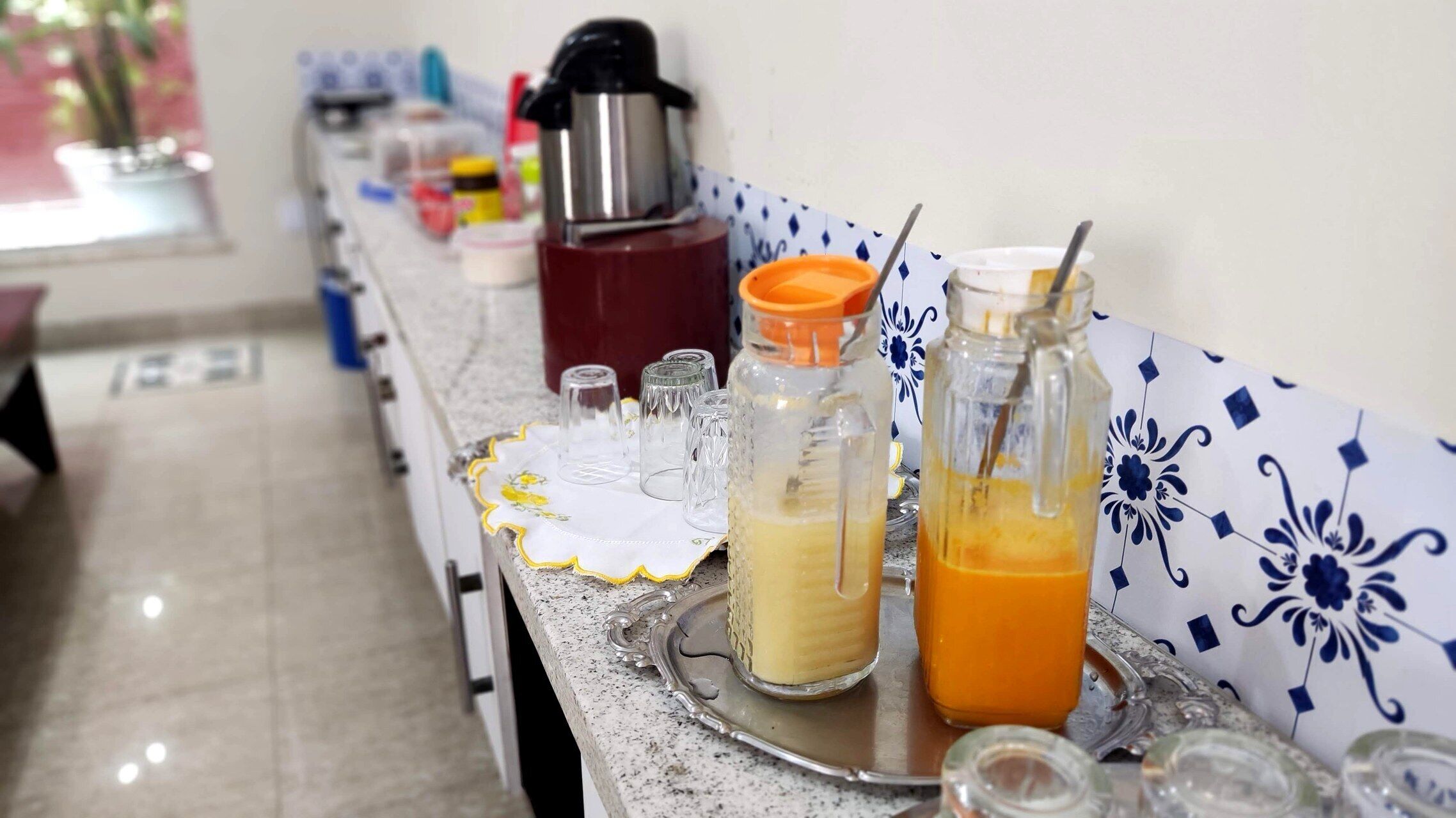 A breakfast bar with various food items and drinks, including a coffee maker, a bottle of orange juice, and a glass of milk.