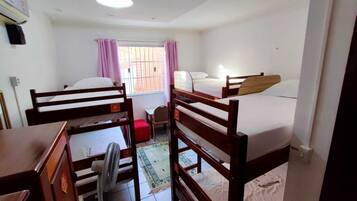 A dormitory room with bunk beds, a desk, a chair, and a small table.