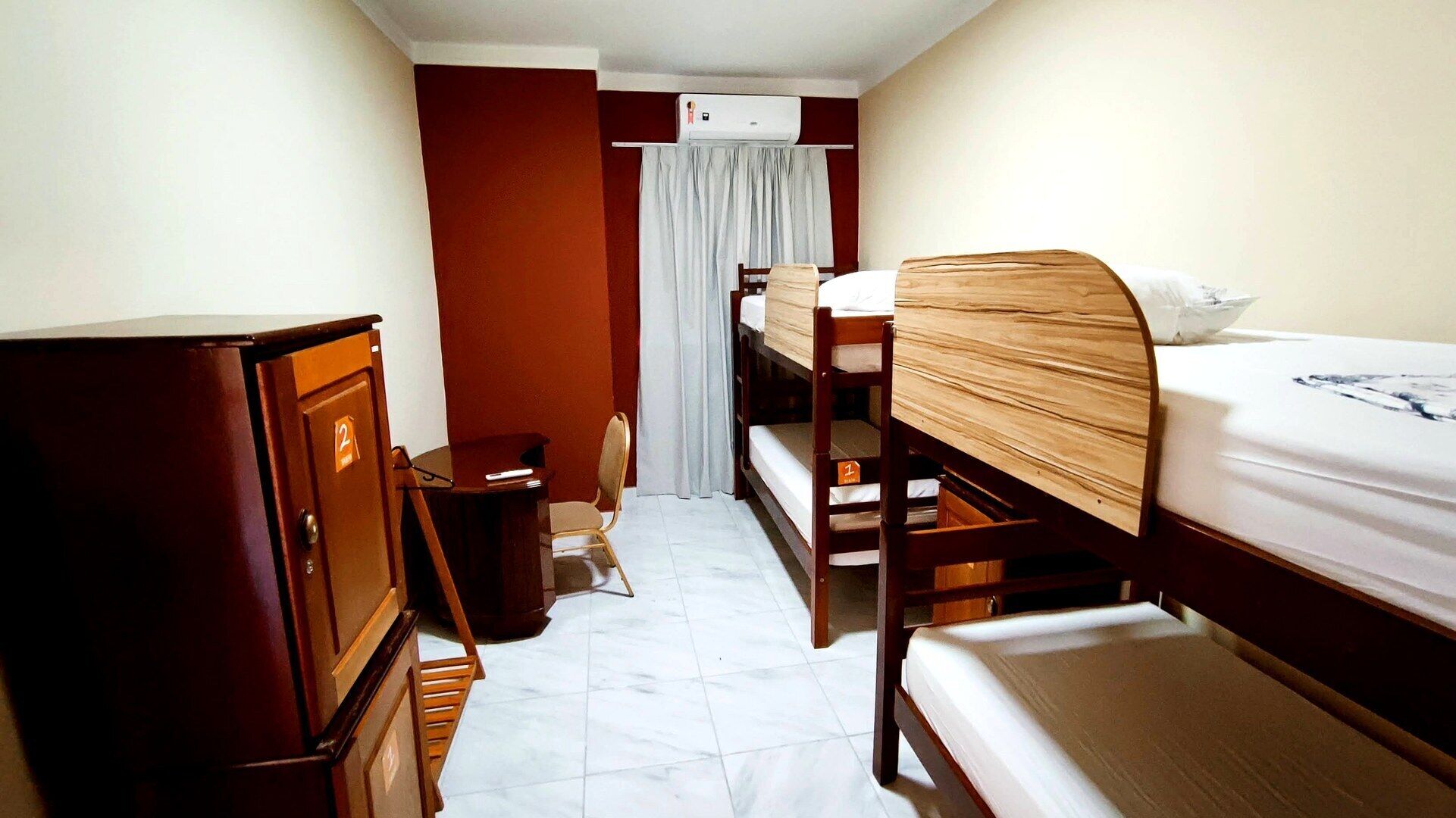 Een kleine, functionele hotelkamer met stapelbedden, een houten garderobe, een bureau en een stoel.
