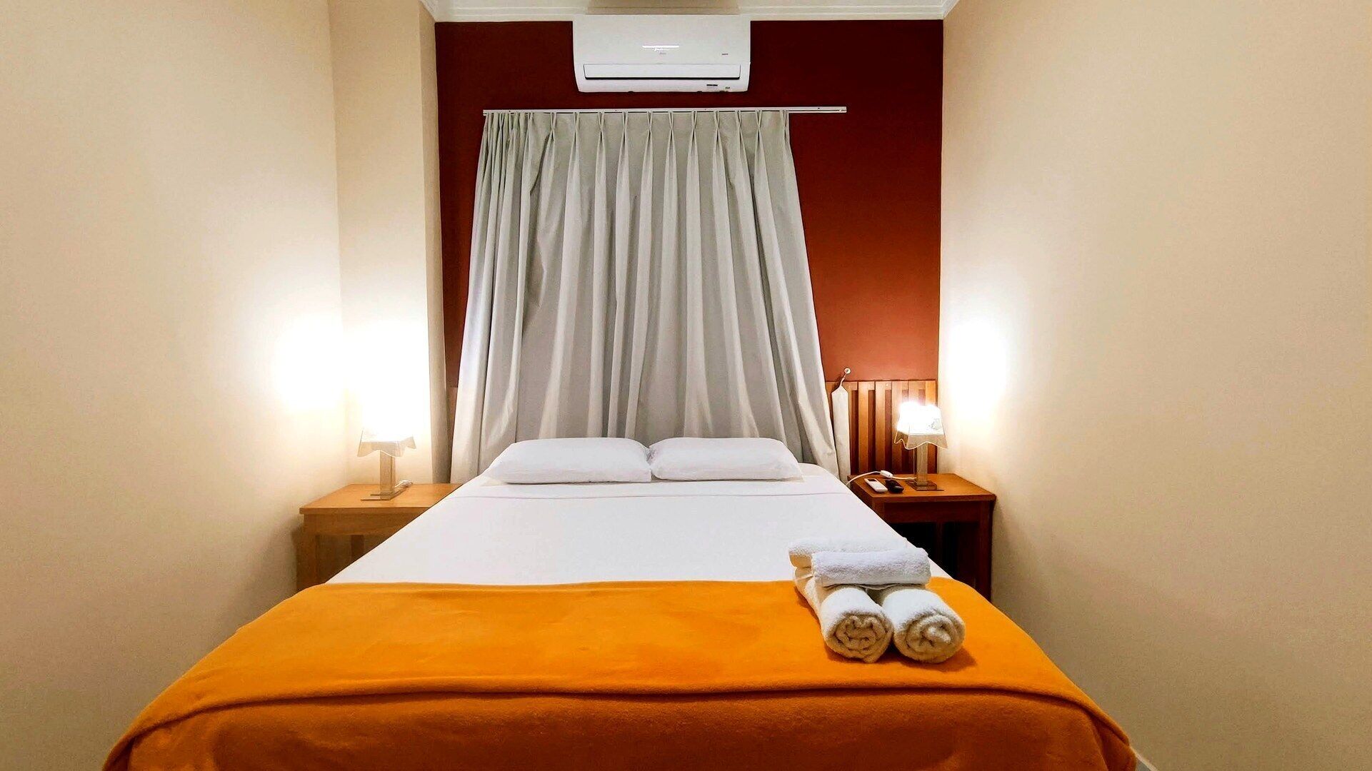 A hotel room with a bed, two bedside tables, a lamp, and a window with curtains.