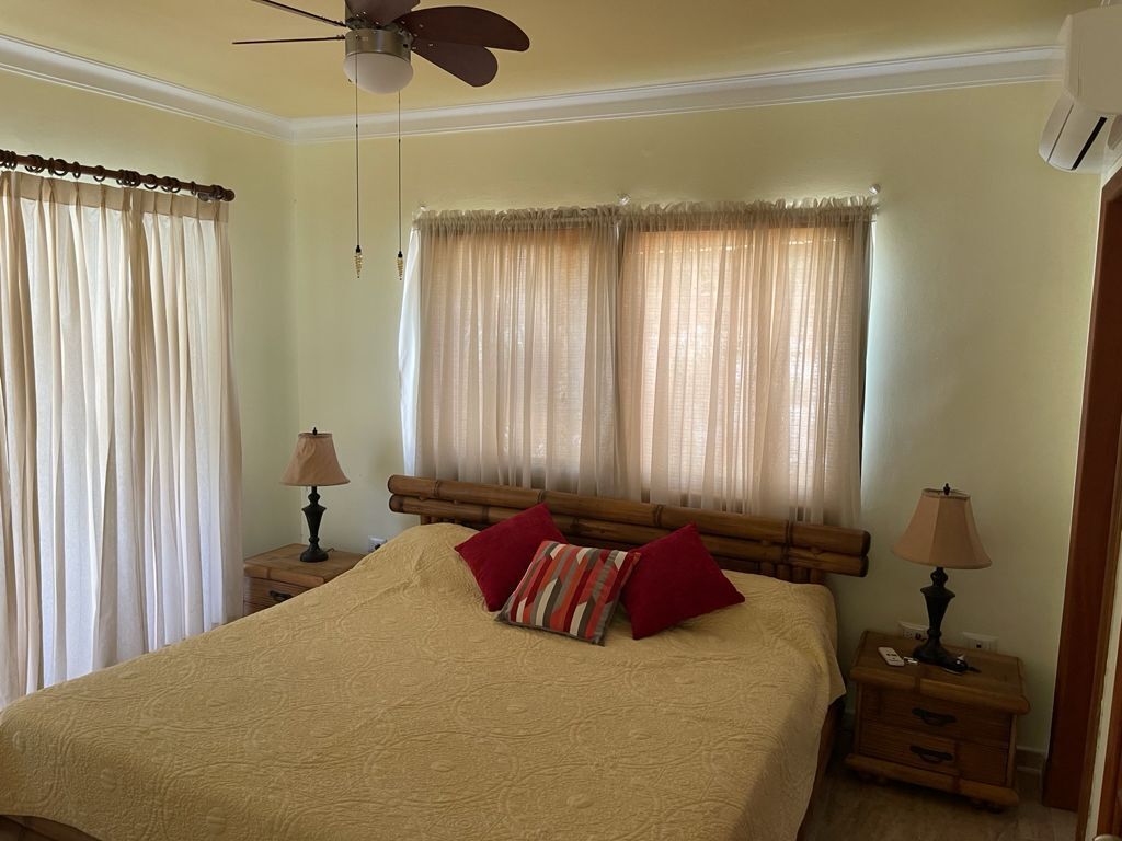 A bedroom with a bed, two bedside tables with lamps, a ceiling fan, and a window with curtains.