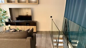 Una sala de estar moderna con un sofá, un televisor, un mueble de madera y una escalera con barandas de vidrio.