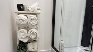 Un baño con un toallero blanco que sostiene toallas dobladas con pulcritud, una botella de jabón para manos y una planta en maceta.