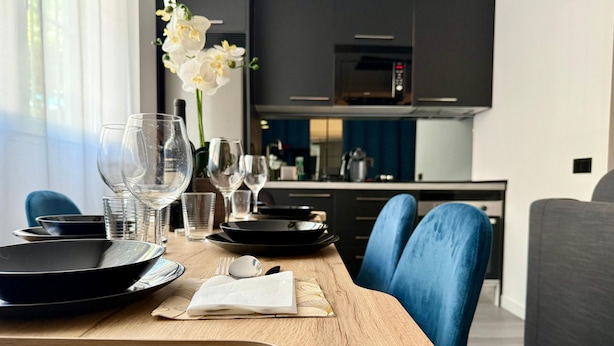 Mesa de comedor dispuesta con platos, vasos y servilleta, rodeada de sillas azules en una cocina moderna.