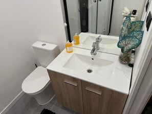 A modern bathroom with a white sink, two faucets, a toilet, and a shower enclosure.
