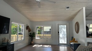 A spacious living room with a ceiling fan, large windows, a television, and a potted plant.