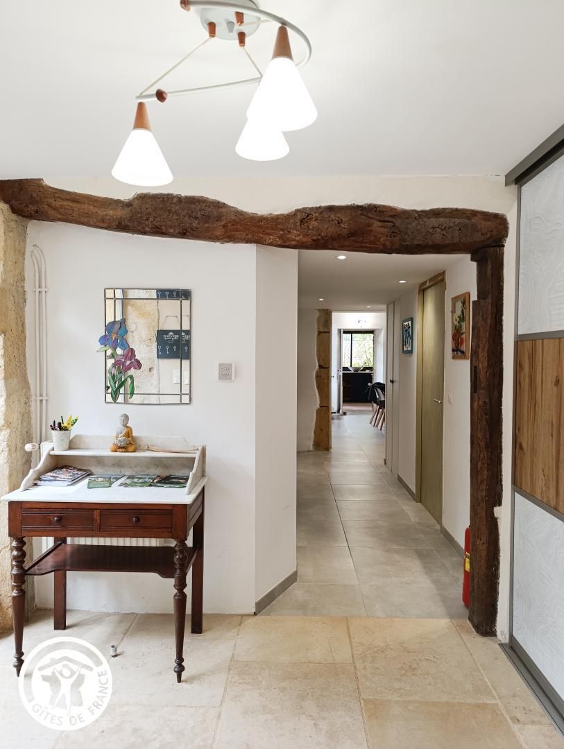 A hallway with a rustic wooden beam ceiling, a marble table with books, and a wall-mounted picture frame.
