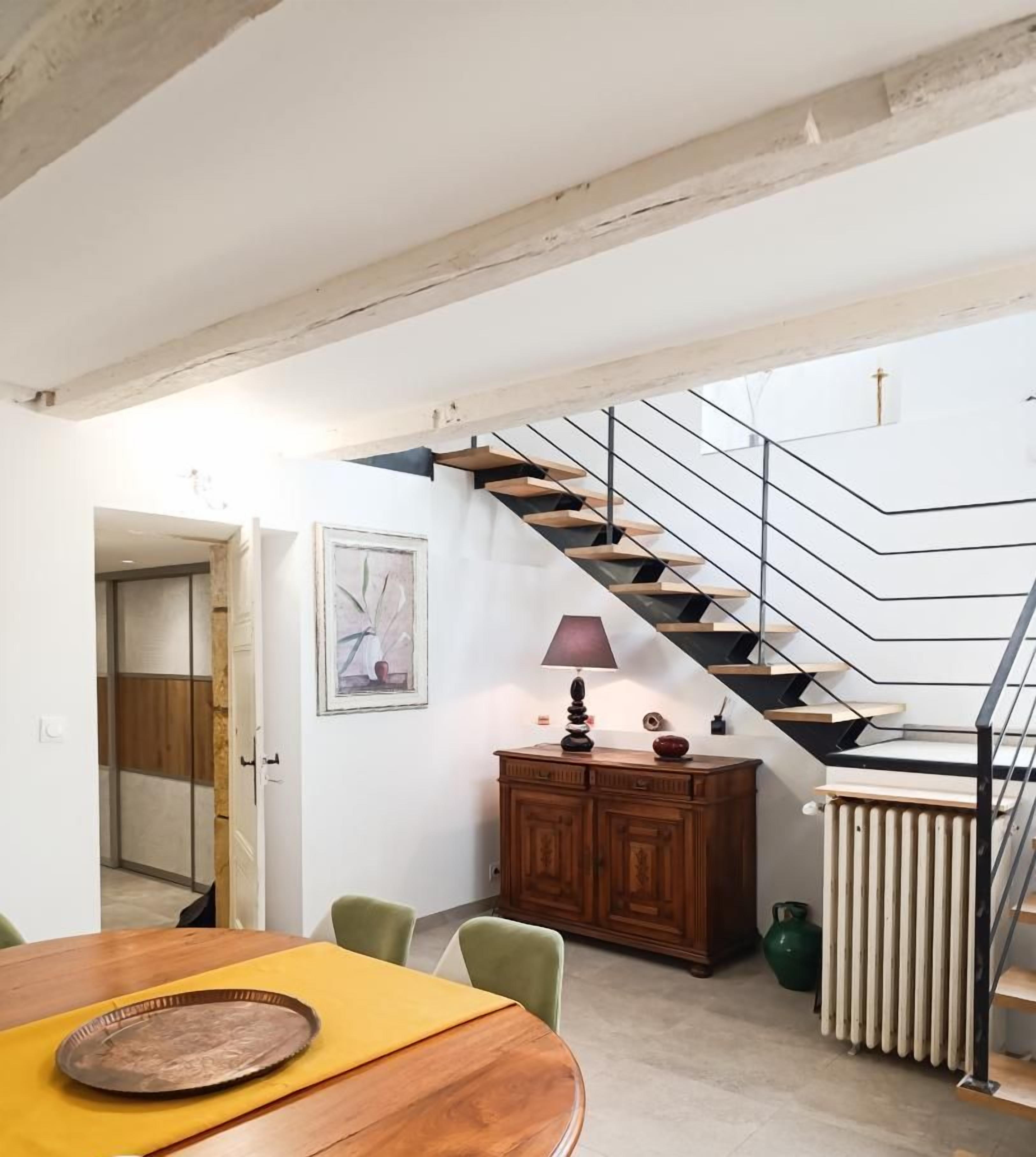 Un coin repas avec une table et des chaises en bois, un escalier au design moderne et un radiateur au sol.
