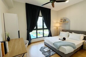 A hotel room with a bed, a desk, a chair, a window with curtains, a ceiling fan, and a nightstand with a lamp. - Splash Mania Homestay (Tanjung Dua Belas)