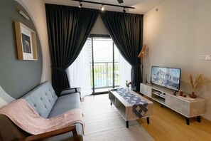 A modern living room with a sofa, a TV, and a balcony view. - Splash Mania Homestay (Tanjung Dua Belas)