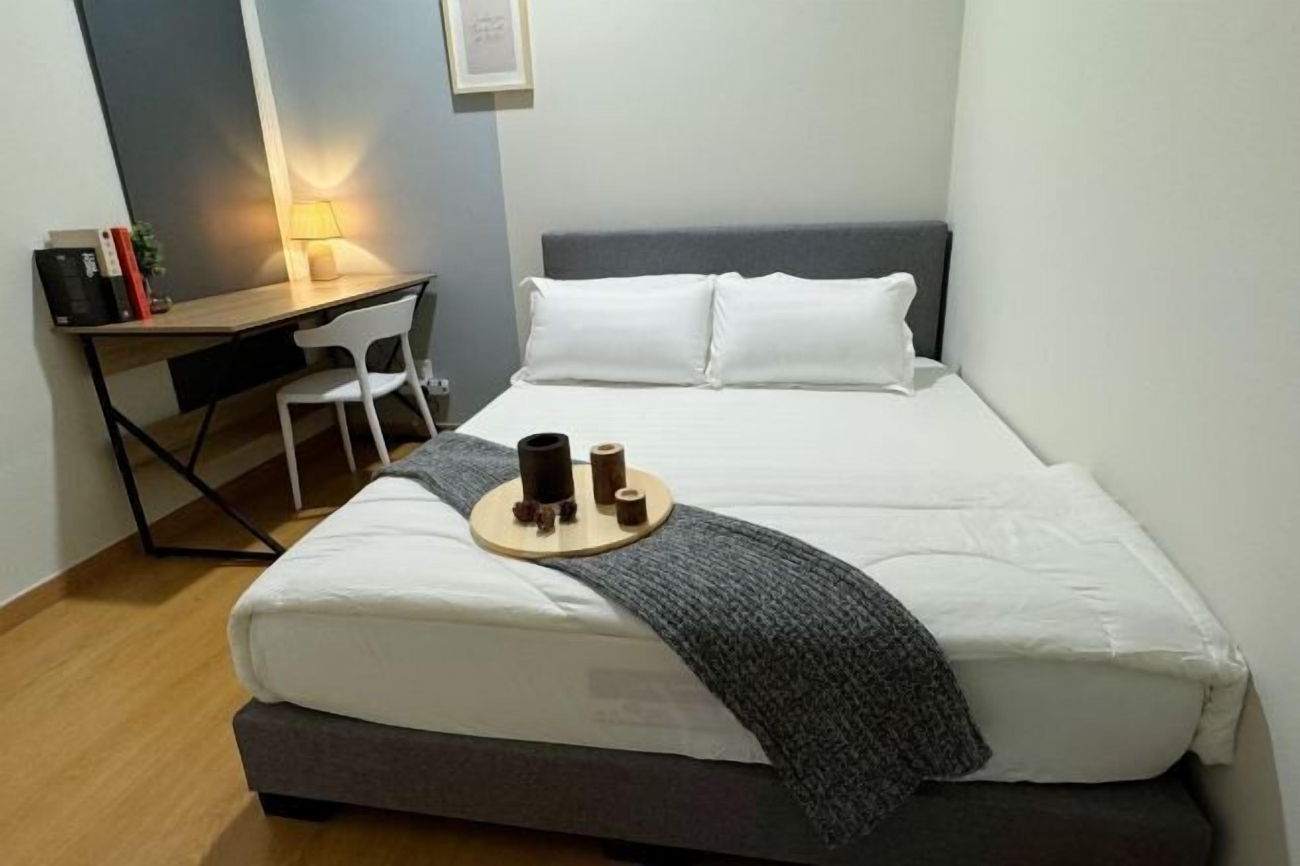 Un dormitorio ordenado con cama, escritorio y silla. Hay una lámpara sobre el escritorio y una bandeja con una taza y un libro sobre la cama.