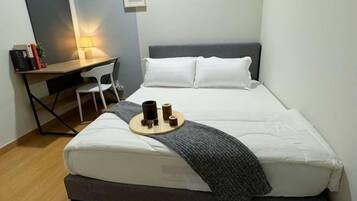 Un dormitorio ordenado con cama, escritorio y silla. Hay una lámpara sobre el escritorio y una bandeja con una taza y un libro sobre la cama.