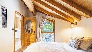 Une chambre avec un plafond en bois, une grande fenêtre avec des rideaux, un lit avec une literie moelleuse et un luminaire fixé au mur.